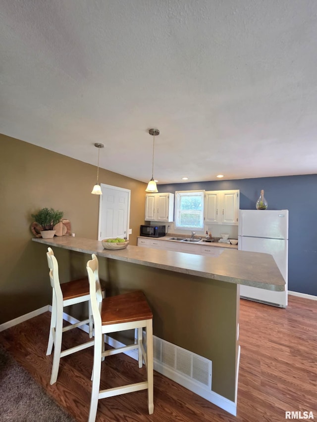 514 W Washington St, Mendon, IL 62351 - kitchen with freestanding refrigerator, black microwave, a kitchen breakfast bar, decorative light fixtures, and a sink