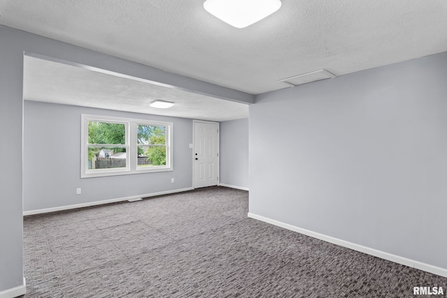 spare room featuring a textured ceiling, carpet floors, baseboards, and attic access