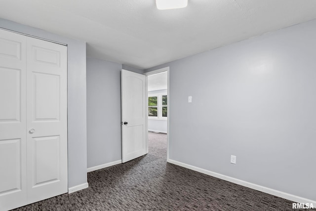 unfurnished bedroom with dark carpet, baseboards, and a closet