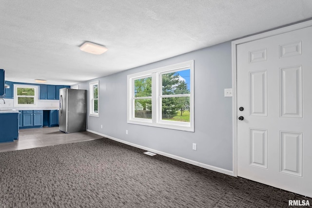 unfurnished living room with a textured ceiling, carpet flooring, and baseboards