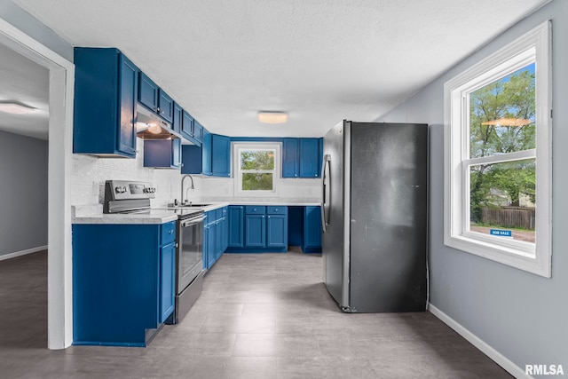 kitchen featuring appliances with stainless steel finishes, blue cabinets, light countertops, under cabinet range hood, and a sink