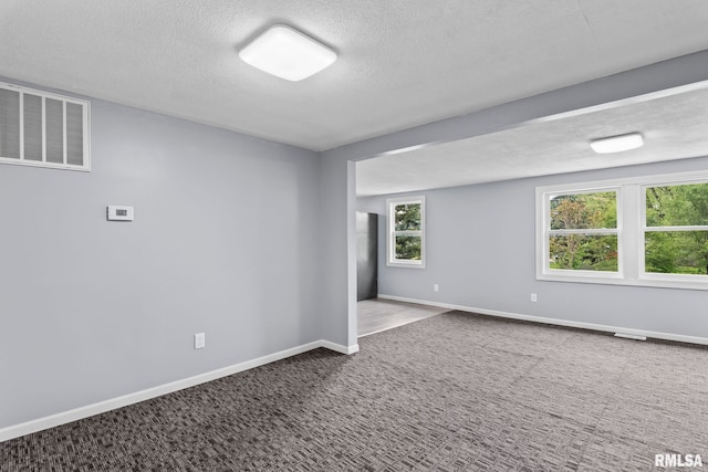 carpeted spare room featuring a textured ceiling and baseboards