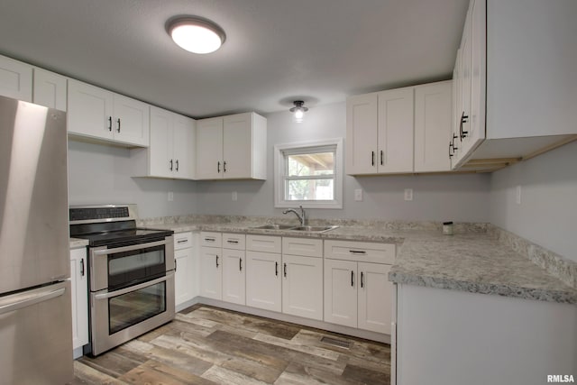 kitchen featuring appliances with stainless steel finishes, a sink, light wood-style flooring, light countertops, and white cabinets