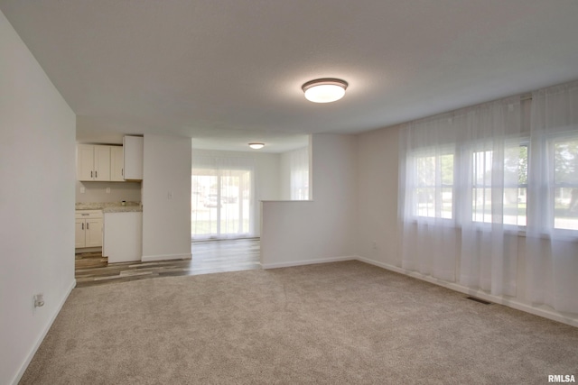 unfurnished living room featuring light colored carpet and baseboards