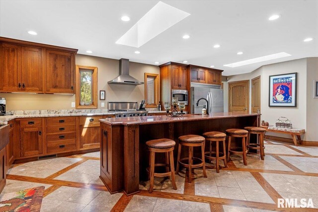 kitchen featuring a skylight, wall chimney exhaust hood, inlaid floor details, appliances with stainless steel finishes, and recessed lighting