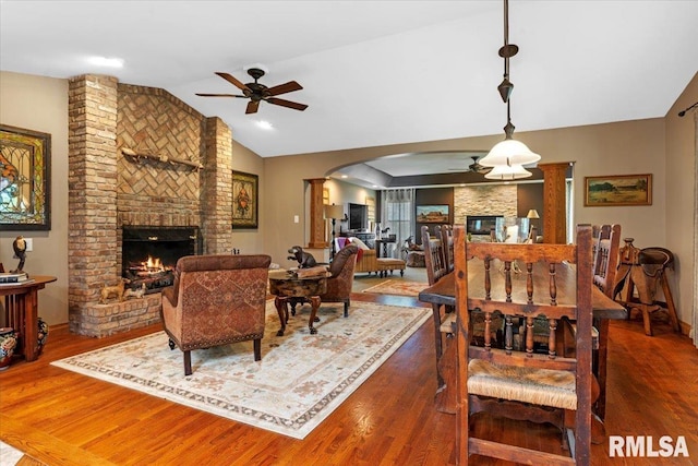living area featuring a brick fireplace, a ceiling fan, wood finished floors, and vaulted ceiling