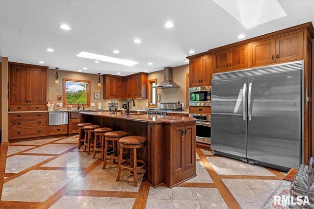 kitchen featuring built in appliances, inlaid floor details, wall chimney exhaust hood, recessed lighting, and brown cabinets