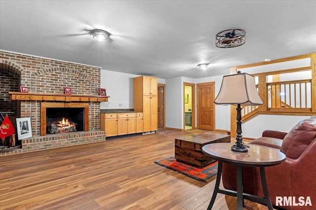 living area featuring wood finished floors, a brick fireplace, baseboards, and stairway