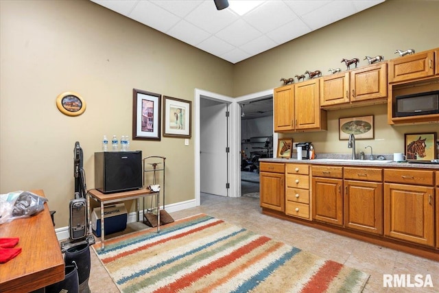 kitchen with a sink, black microwave, light countertops, brown cabinets, and a drop ceiling