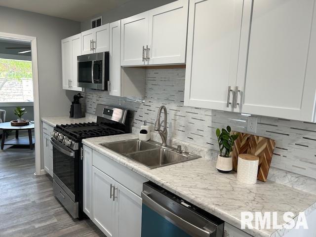 818 Van Buren St, Quincy, IL 62301 - kitchen featuring appliances with stainless steel finishes, a sink, white cabinets, decorative backsplash, and light wood-style floors