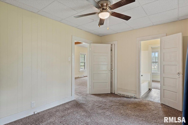 708 E 5th St, Pana, IL 62557 - unfurnished bedroom featuring carpet flooring, multiple windows, wooden walls, a paneled ceiling, and a ceiling fan