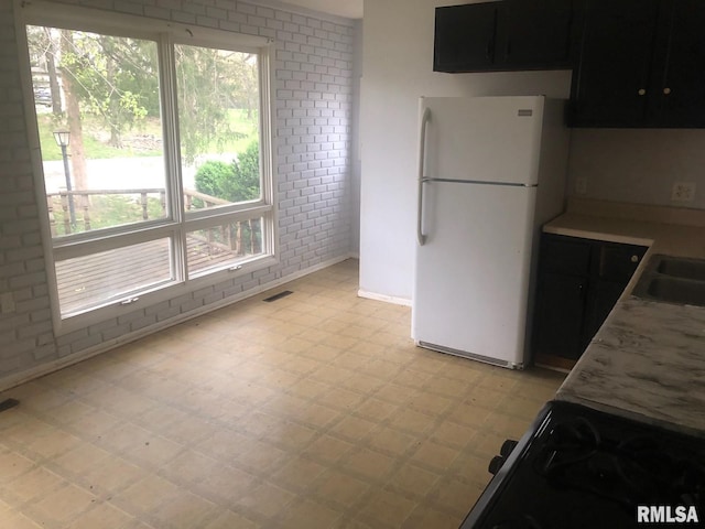 1522 Rim Rd, Quincy, IL 62305 - kitchen featuring freestanding refrigerator, light flooring, brick wall, black gas range oven, and dark cabinets