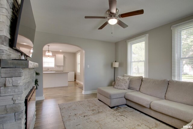 801 S 22nd St, Quincy, IL 62301 - living area with arched walkways, a ceiling fan, light wood-type flooring, baseboards, and a stone fireplace