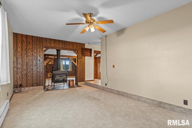 34831 Greenland Rd, Virden, IL 62690 - unfurnished living room featuring a baseboard heating unit, carpet floors, a wood stove, a ceiling fan, and wood walls