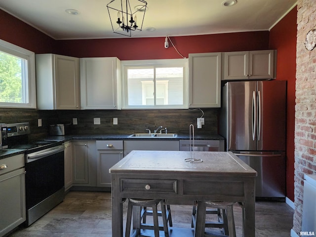 kitchen featuring appliances with stainless steel finishes, a sink, backsplash, dark countertops, and pendant lighting