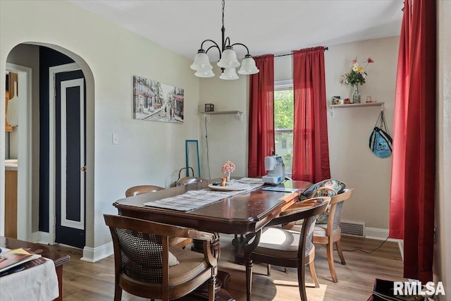 dining room with arched walkways, a chandelier, baseboards, and light wood-style floors
