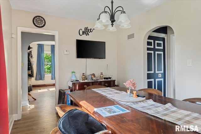 dining room featuring arched walkways, a chandelier, wood finished floors, and baseboards