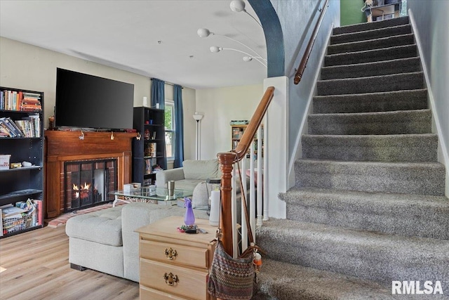 living area featuring stairway, wood finished floors, and a lit fireplace