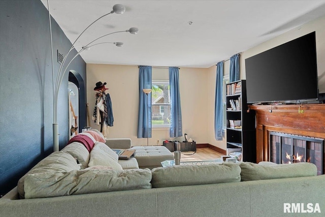 living room featuring a warm lit fireplace, arched walkways, and baseboards