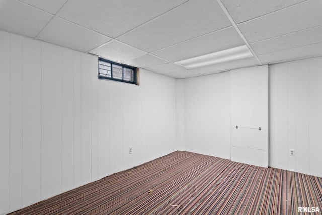 basement featuring a paneled ceiling, a decorative wall, and carpet