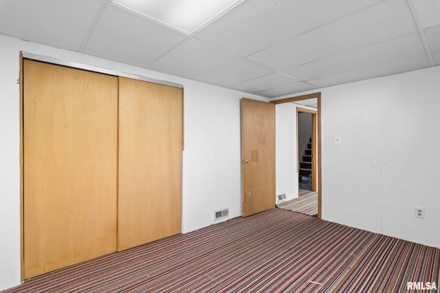 unfurnished bedroom featuring a drop ceiling, a closet, and carpet flooring