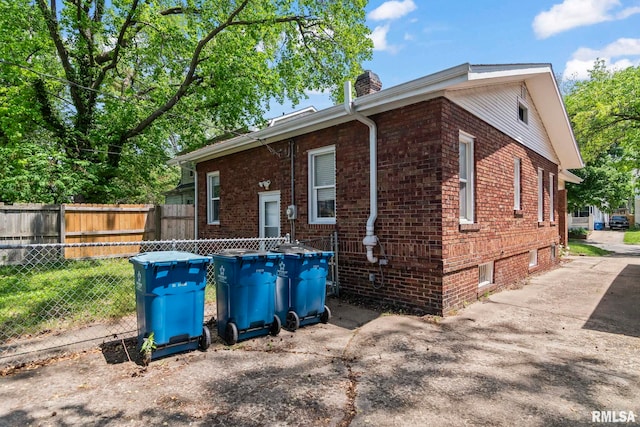 view of side of property with brick siding, a chimney, and fence