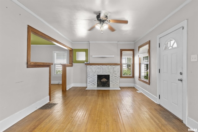 unfurnished living room with ceiling fan, light wood finished floors, a brick fireplace, baseboards, and ornamental molding