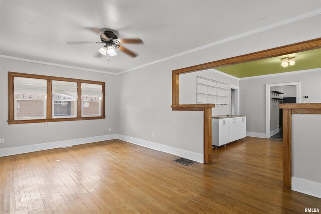 empty room featuring a ceiling fan, wood-type flooring, baseboards, and crown molding