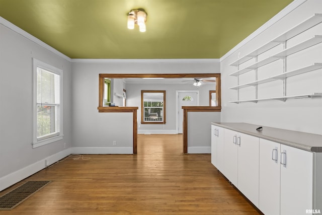 corridor featuring baseboards, light wood-style flooring, healthy amount of natural light, and ornamental molding