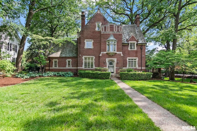 tudor home with a chimney, a front lawn, and brick siding