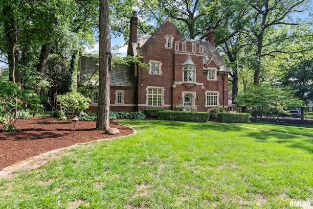 english style home featuring a front lawn, a chimney, and brick siding