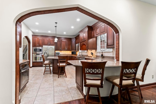 kitchen with stainless steel appliances, arched walkways, a kitchen breakfast bar, decorative backsplash, and a peninsula