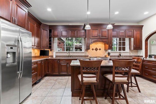 kitchen featuring appliances with stainless steel finishes, a sink, decorative backsplash, arched walkways, and light tile patterned flooring