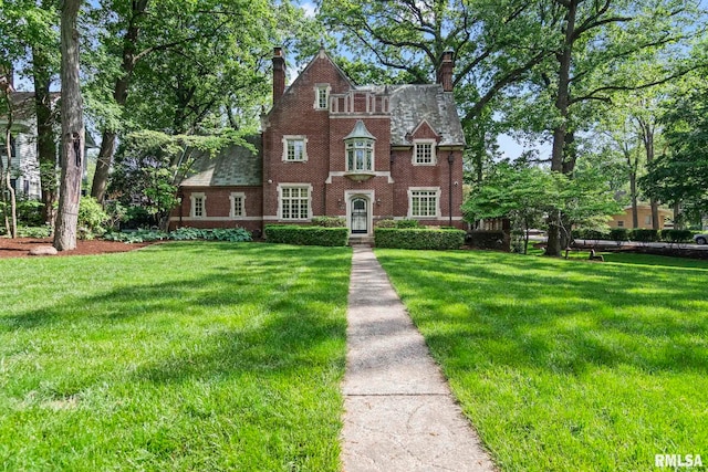 tudor home featuring a front lawn, a chimney, and brick siding