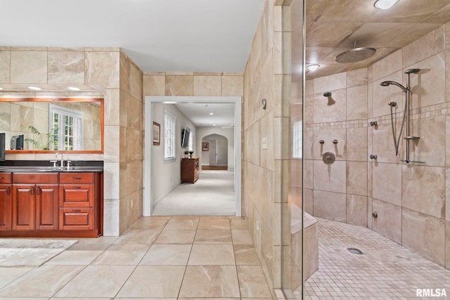 full bath with tiled shower, tile patterned floors, vanity, and tile walls