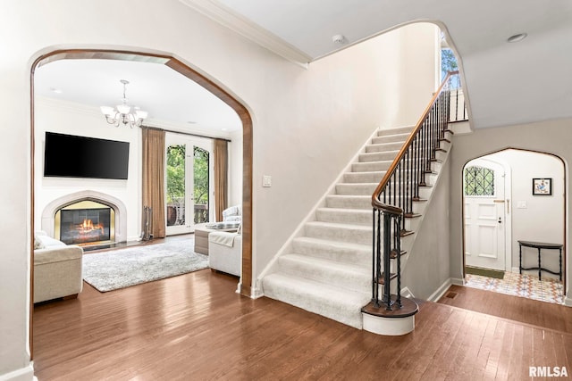 foyer entrance with hardwood / wood-style floors, arched walkways, a chandelier, stairway, and baseboards