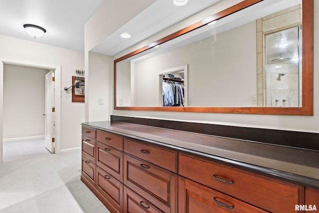 full bathroom with vanity, baseboards, a walk in closet, and a tile shower