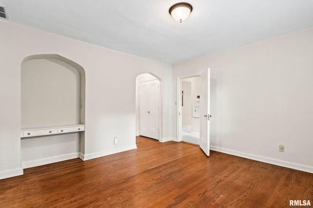 spare room with wood finished floors, arched walkways, and baseboards
