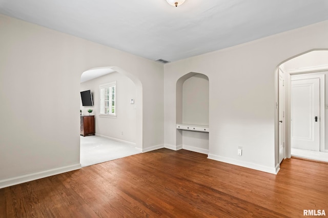 unfurnished room featuring wood finished floors, arched walkways, and baseboards
