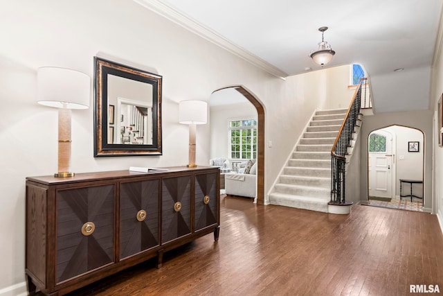 entrance foyer featuring arched walkways, ornamental molding, stairway, wood finished floors, and baseboards