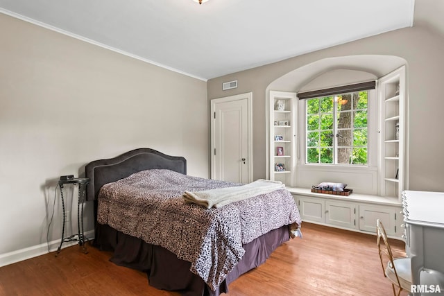 bedroom with light wood finished floors, crown molding, and baseboards