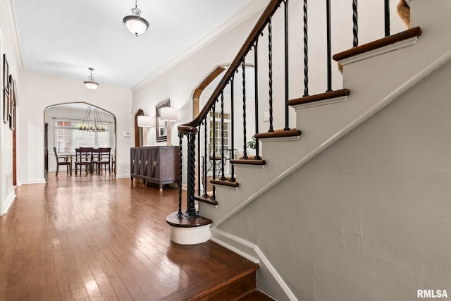 foyer with arched walkways, baseboards, wood-type flooring, stairs, and crown molding