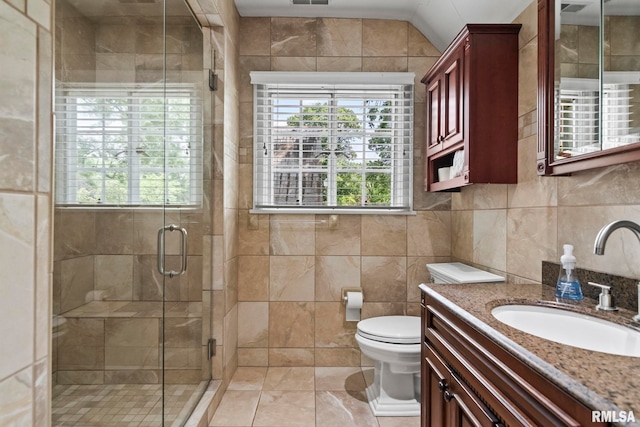 bathroom with tile walls, a shower stall, vanity, and toilet