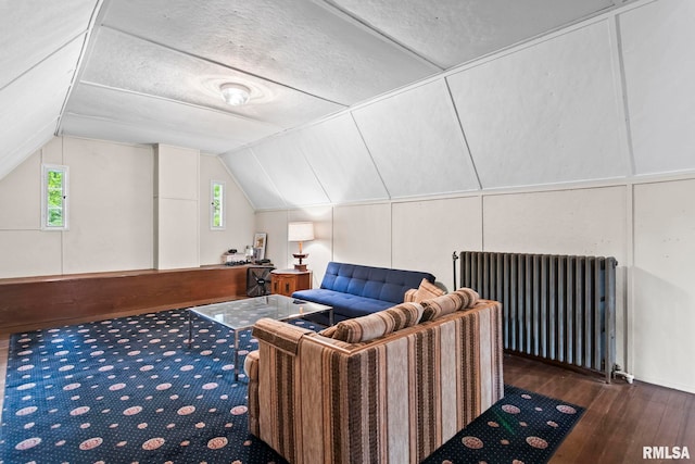 sitting room featuring radiator heating unit, wood finished floors, lofted ceiling, and a decorative wall