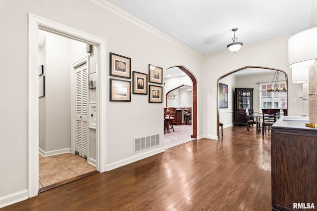 entrance foyer featuring arched walkways, ornamental molding, dark wood-style flooring, and baseboards