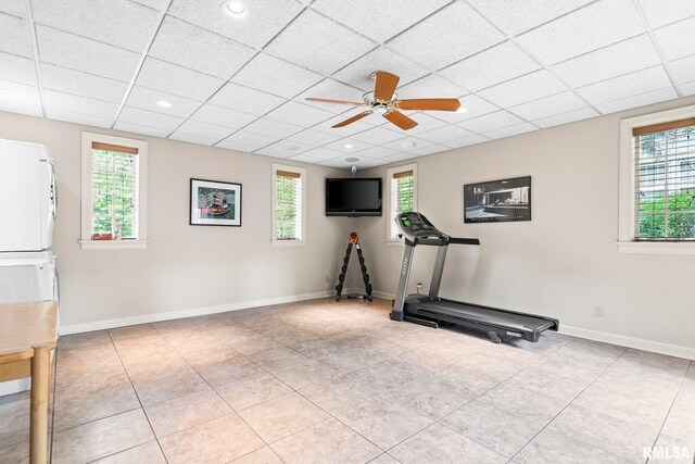 workout room with stacked washer / dryer, a ceiling fan, tile patterned flooring, a drop ceiling, and baseboards