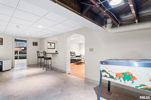 game room featuring baseboards, arched walkways, finished concrete floors, recessed lighting, and a drop ceiling