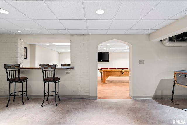 kitchen with baseboards, billiards, a drop ceiling, a kitchen breakfast bar, and finished concrete flooring