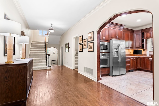 kitchen with stainless steel appliances, arched walkways, ornamental molding, light wood finished floors, and baseboards