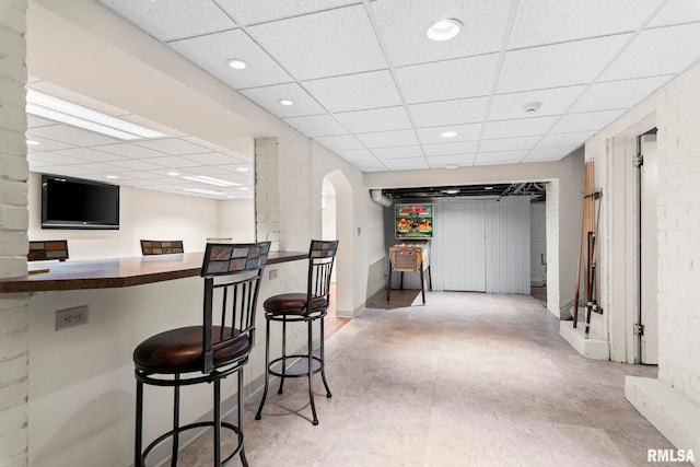 bar area featuring a drop ceiling, concrete floors, arched walkways, recessed lighting, and baseboards
